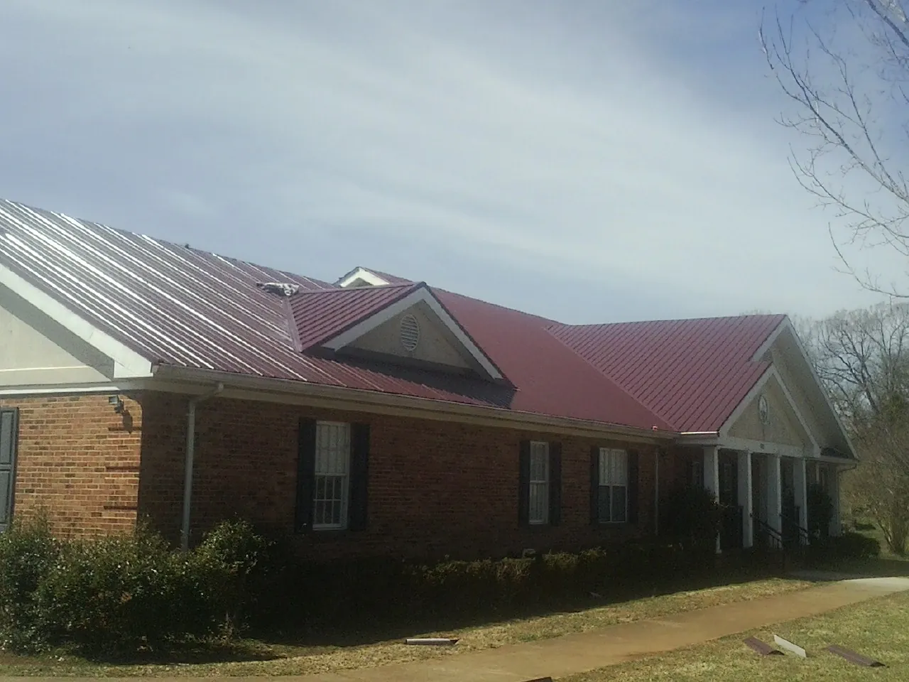Red metal roof with gabled entries on a long brick building, from a Hail Damage Roof Repair job in Kings Mountain