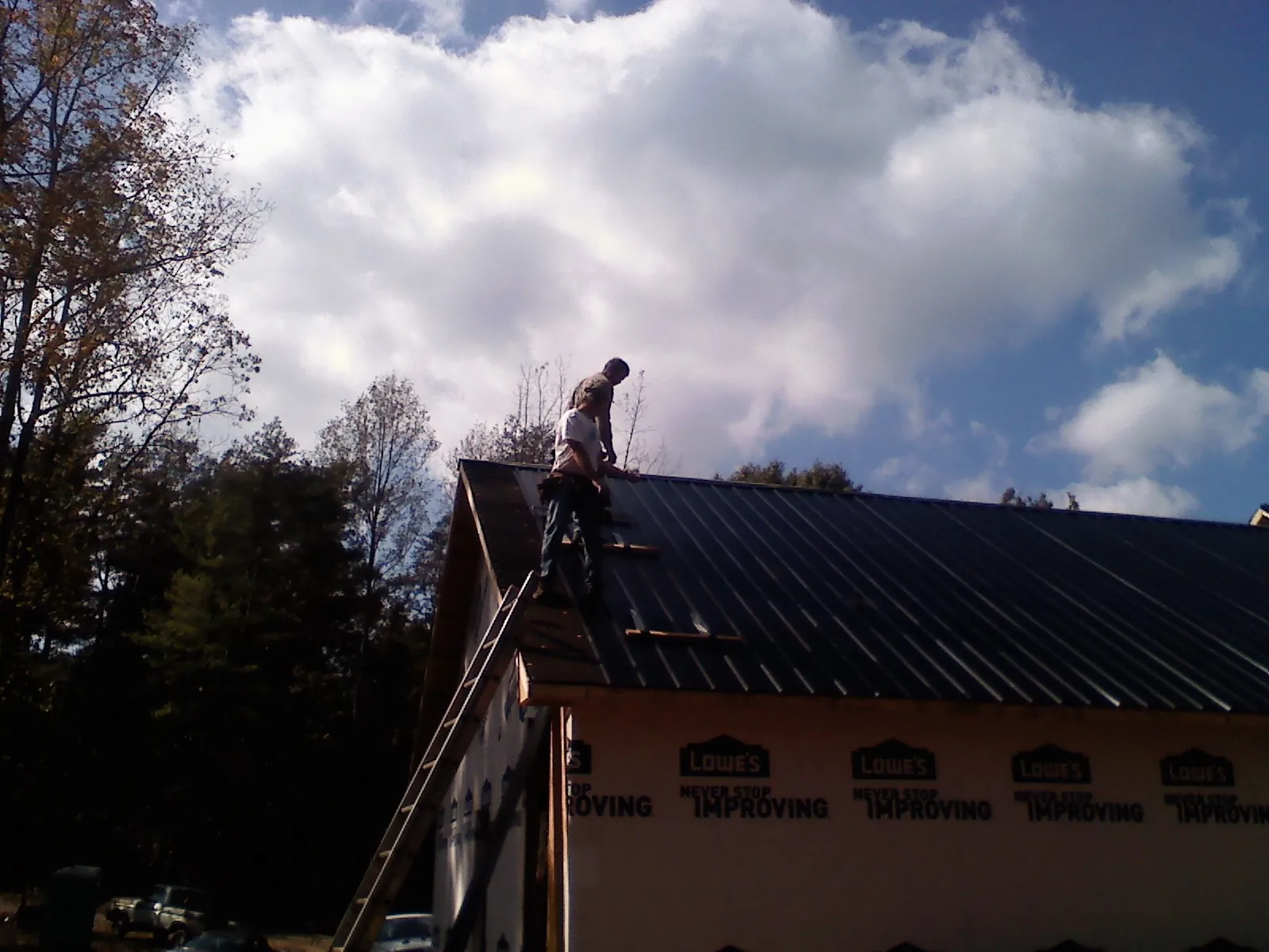 Roofer fastening dark metal panels high against a cloudy sky, from a Roof Inspection job in Kings Mountain
